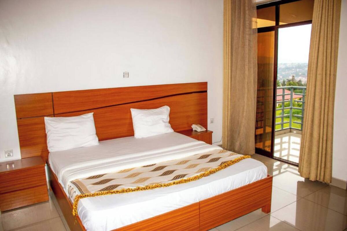 Habitación de hotel con cama de madera, mesita de noche y ventana grande con vistas a zonas verdes.