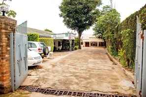 A paved driveway leading to a reception area with a sign, parked cars, and a tree.