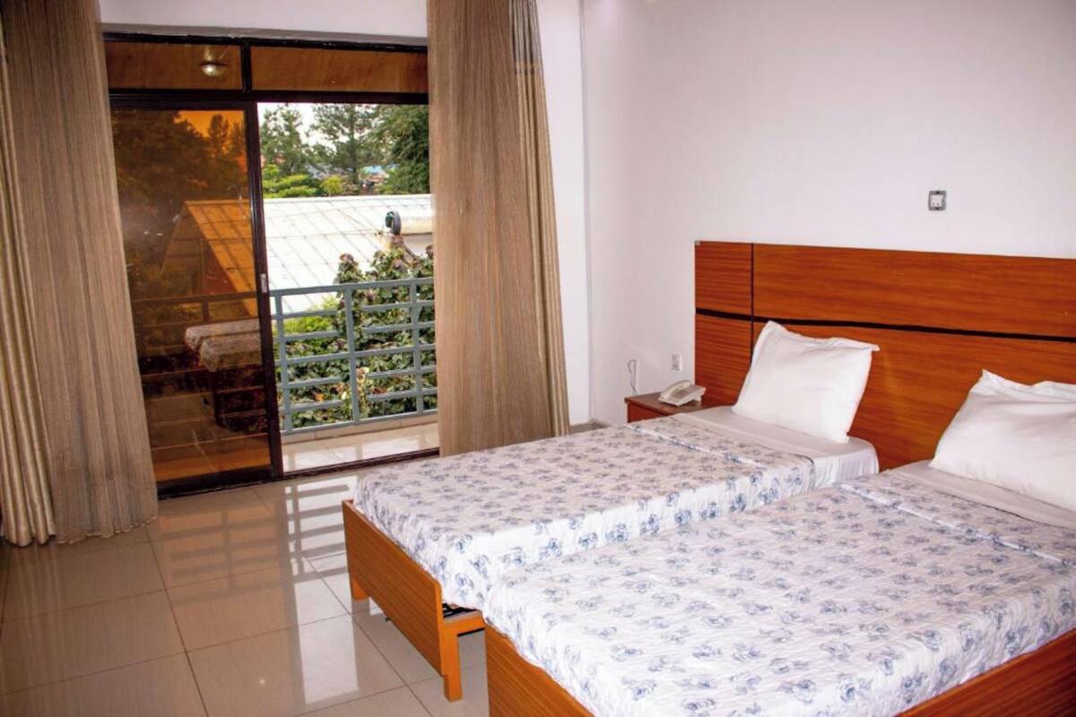 Habitación de hotel con cama de madera, mesita de noche y vista a un balcón con plantas.
