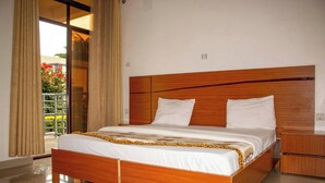 Moderni hotellihuone, jossa on puinen sänky, yöpöytä ja näkymä kukilla koristellulle parvekkeelle.