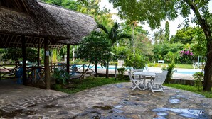 A stone patio with a thatched-roof structure, outdoor seating, and a pool area. - Greenwood Resort (Mtwapa)