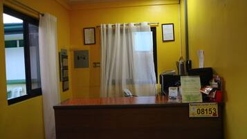 A reception area with a wooden counter, a telephone, a business license plate, and a window with a curtain.