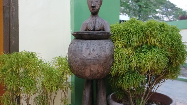 Una estatua con un cuenco en la cabeza, dos plantas en macetas y un suelo de baldosas.