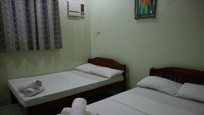 Una habitación con dos camas individuales, cada una con ropa blanca y almohadas, un cabecero de madera y una mesita con una toalla enrollada.