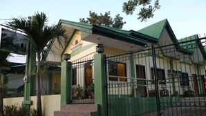 Una casa de dos pisos con techo verde y entrada protegida por una reja.
