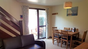 A living room with a sofa, wooden dining table, chairs, and a staircase. - Tolroy Manor Holiday Park (Hayle)