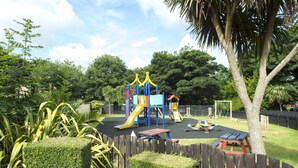 A playground with slides and climbing structures, surrounded by a wooden fence and greenery. - Tolroy Manor Holiday Park (Hayle)