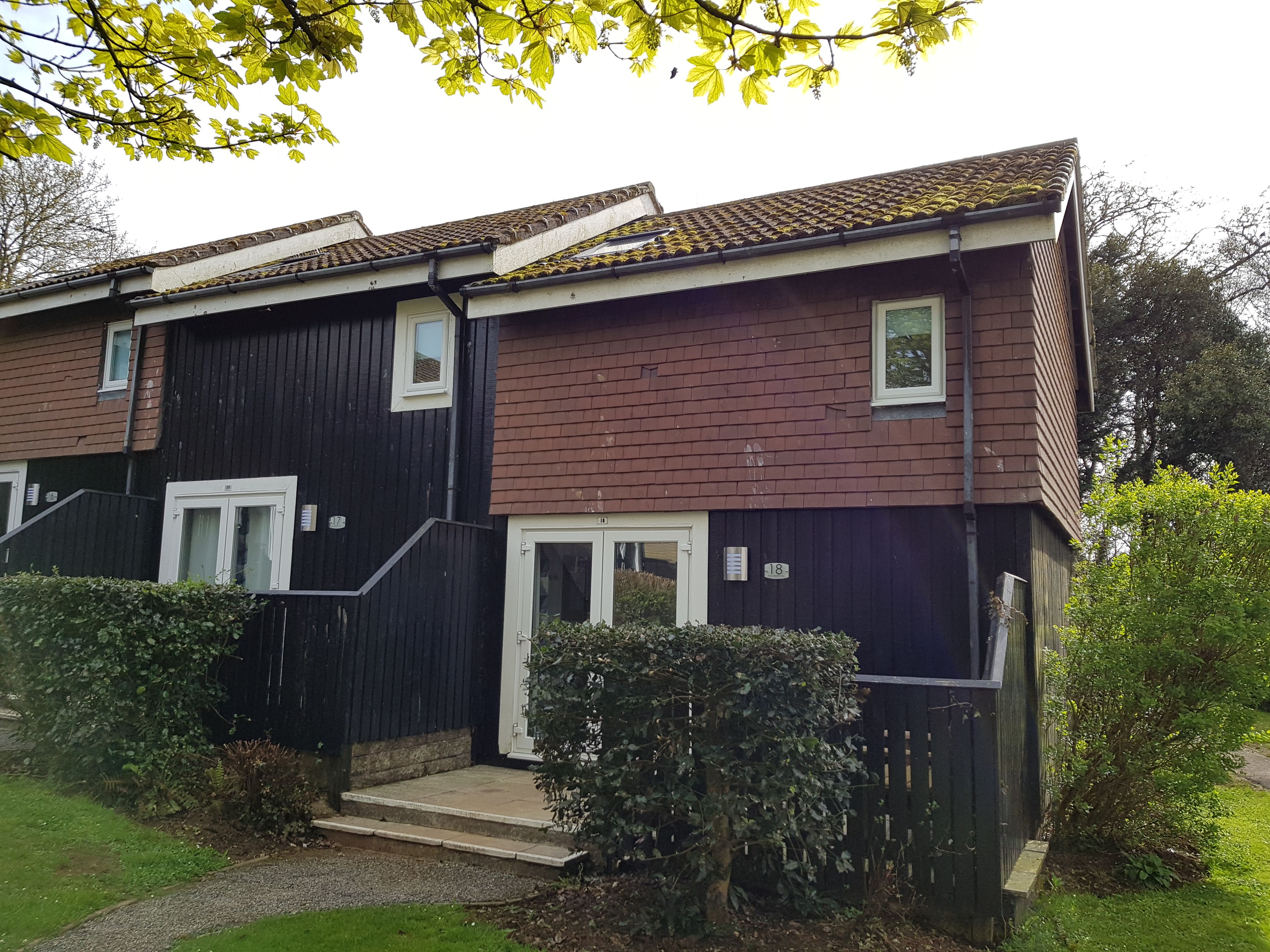 A two-story residential building with a dark facade, white-framed windows, and a tiled roof.