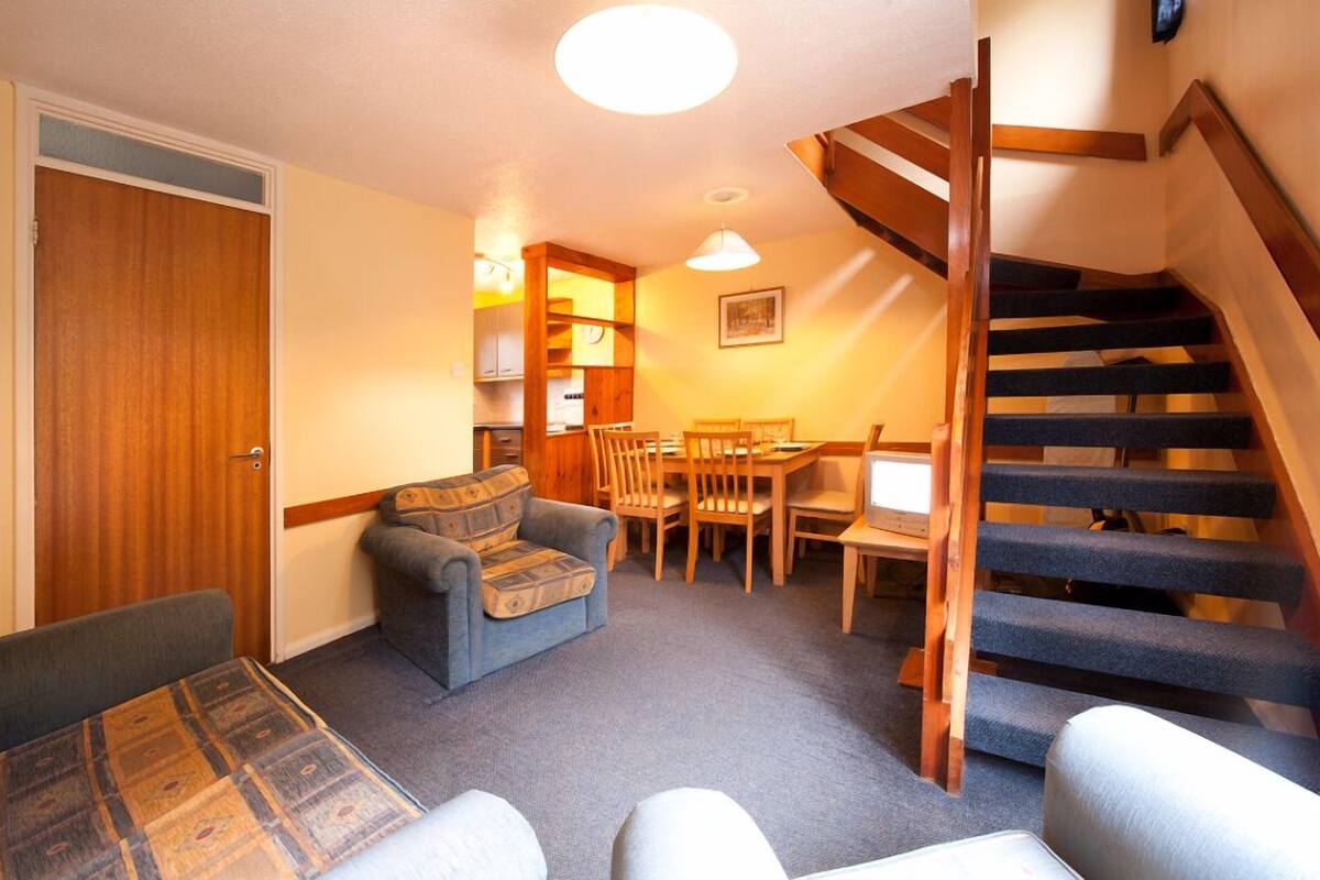 Un espace de vie compact comprenant un coin repas, un canapé, un escalier et une porte en bois.
