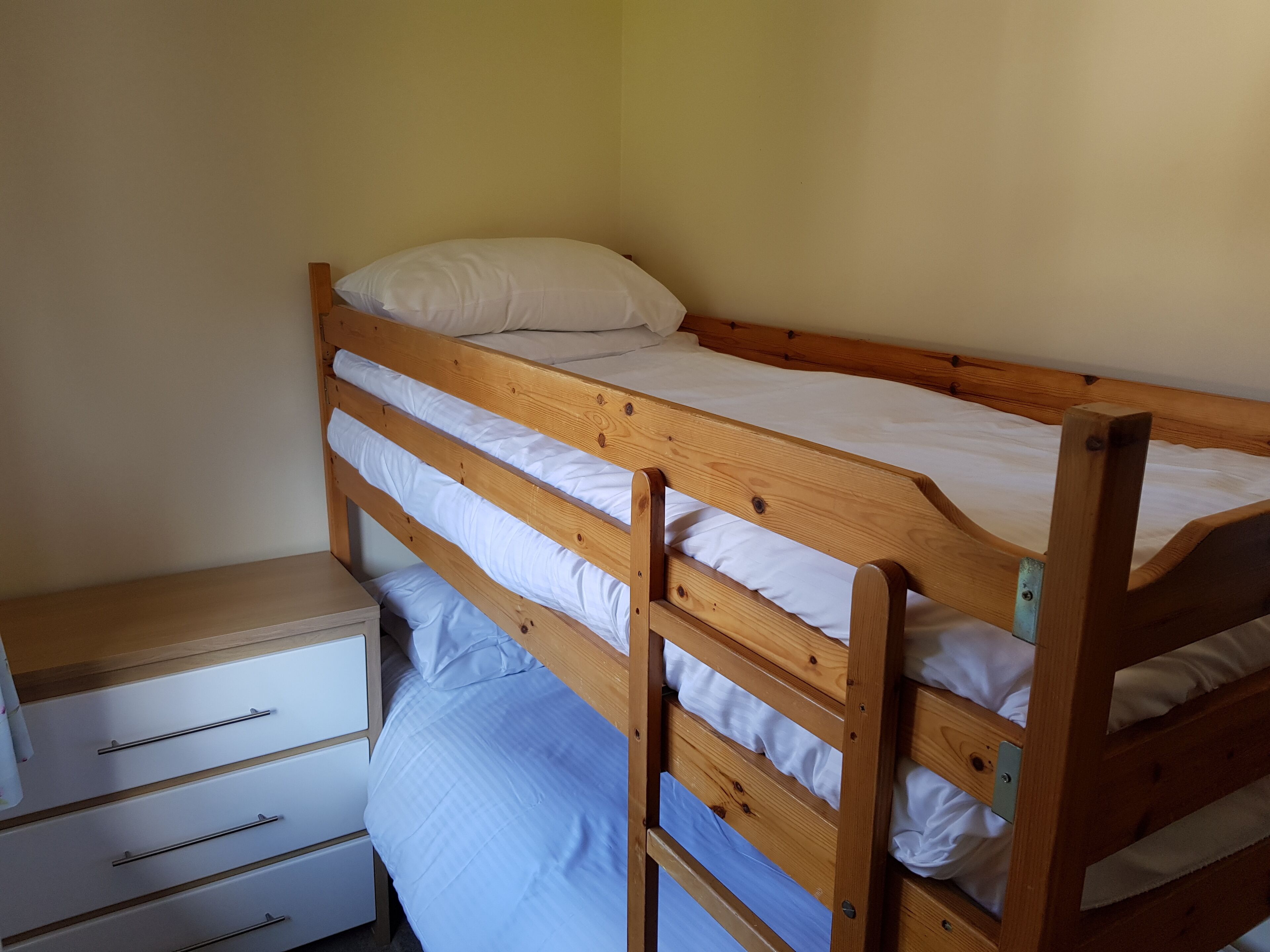 A bunk bed with a wooden frame and white bedding.