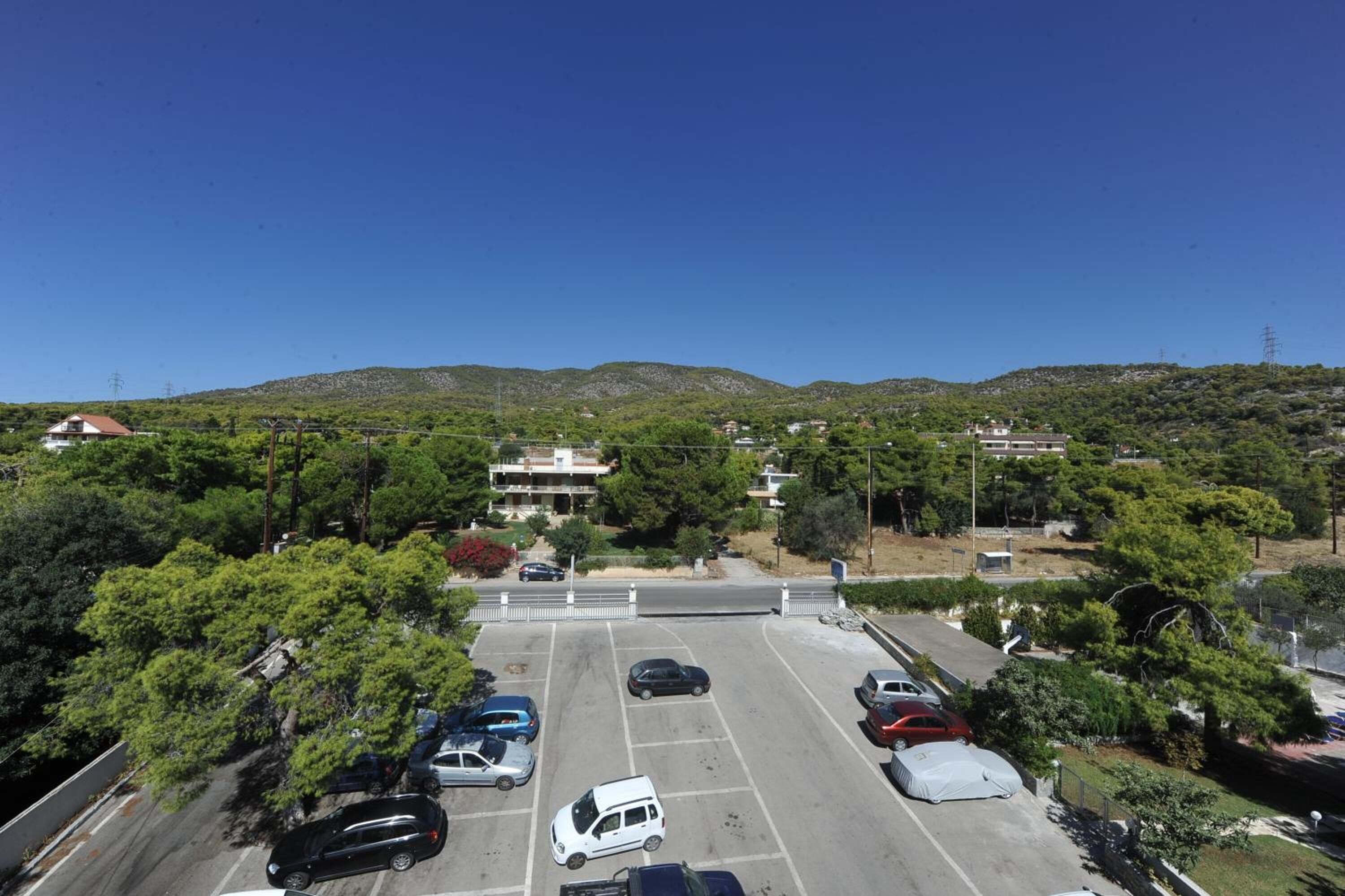 A parking lot with several cars, surrounded by greenery and hills in the background.