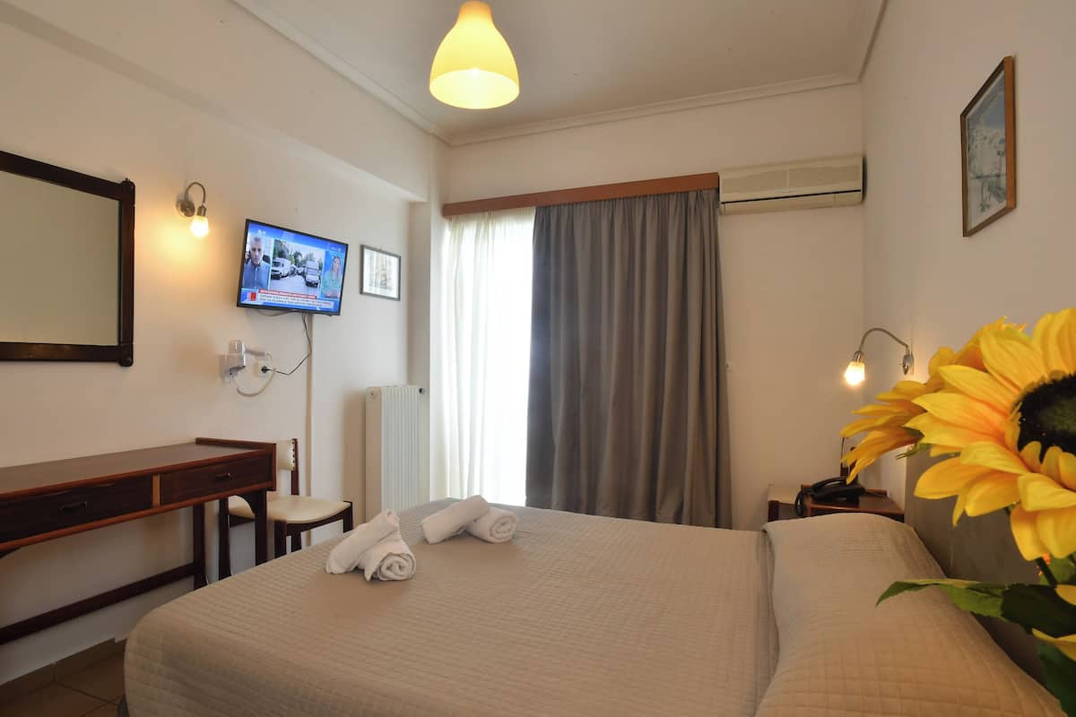 Habitación de hotel con cama, escritorio, silla, televisor y un amplio ventanal con cortinas.