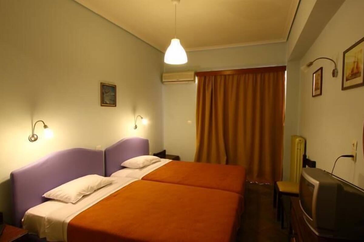 Una habitación de hotel con cama doble, televisión, espejo y ventana con cortinas.