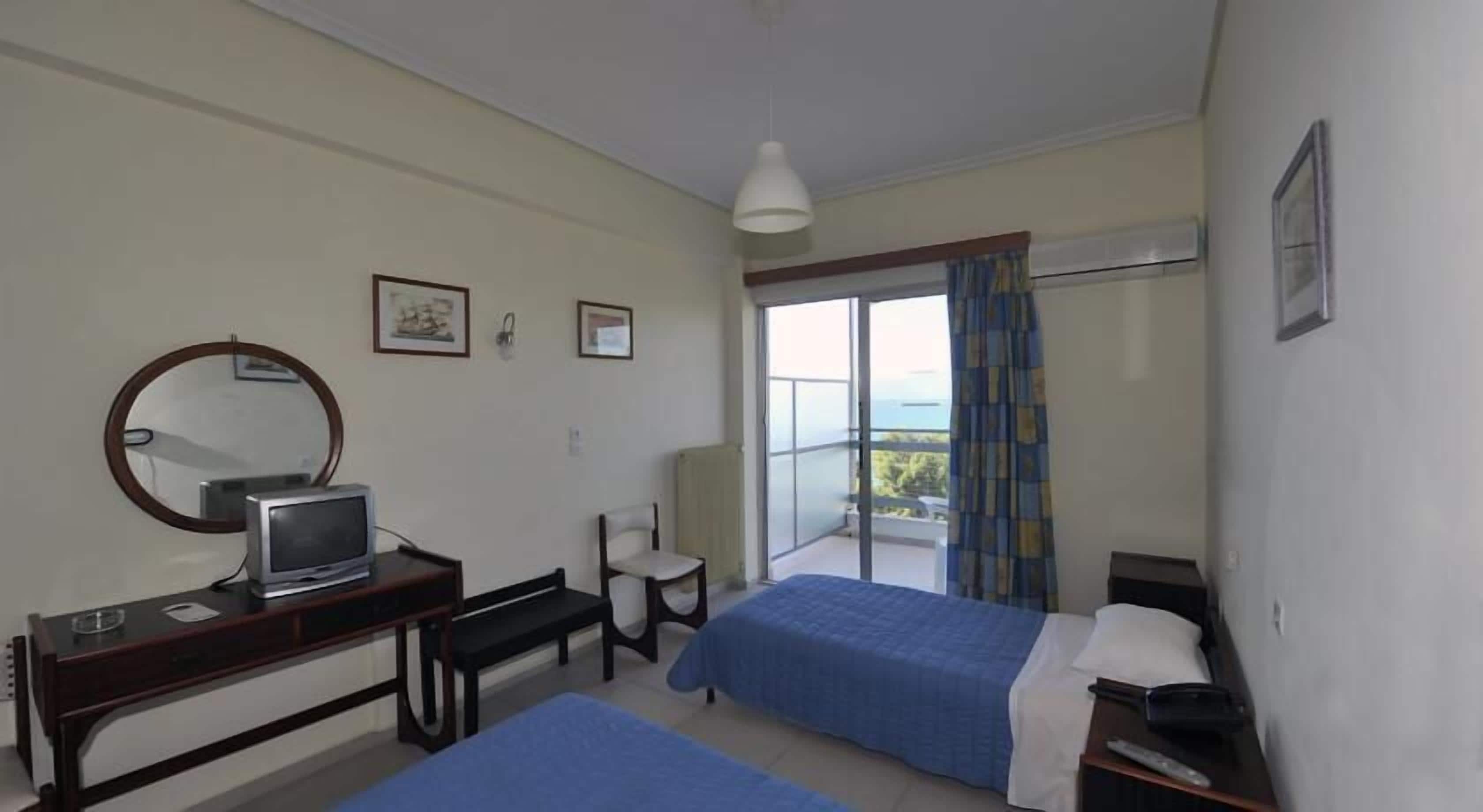 Habitación de hotel con dos camas, un escritorio con computadora, una silla, una ventana con vistas y una lámpara en el techo.