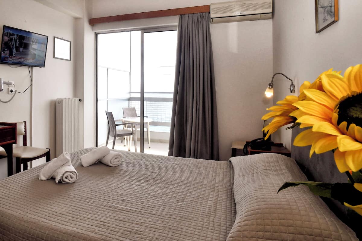 Una habitación de hotel con cama, una silla, una mesa, un televisor y un ventanal con cortinas.