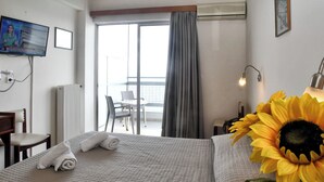 Habitación de hotel con cama, televisión, una silla, una mesa, ventana con cortinas y vistas al exterior.