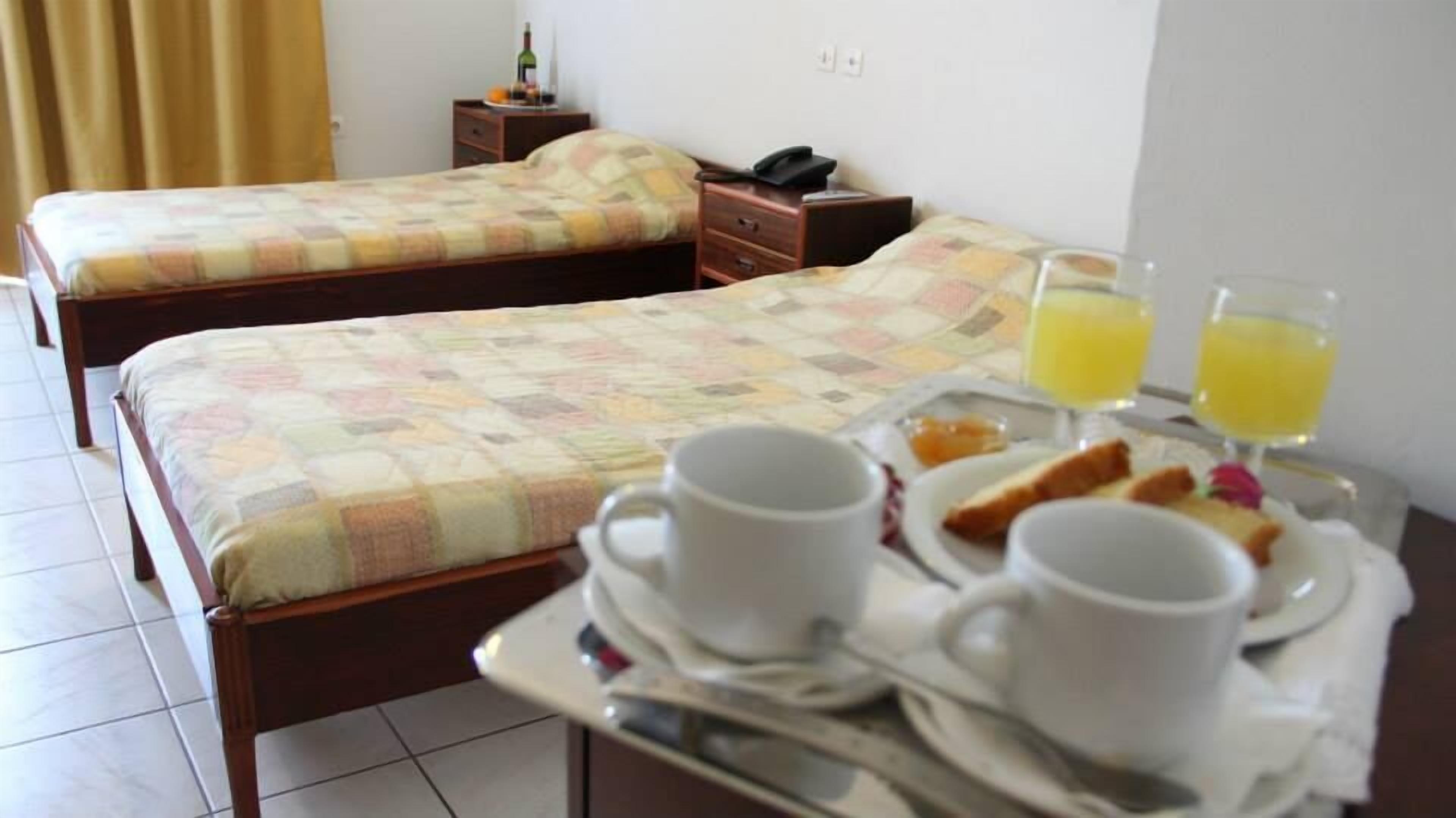 Hotelkamer met twee bedden, een nachtkastje met een telefoon, en een ontbijttray met bekers en sinaasappelsap.