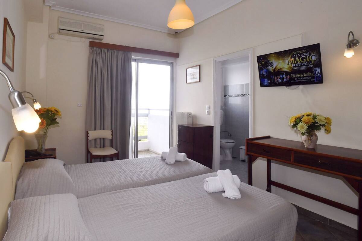 Habitación de hotel con dos camas, televisión, escritorio, silla, baño y balcón.