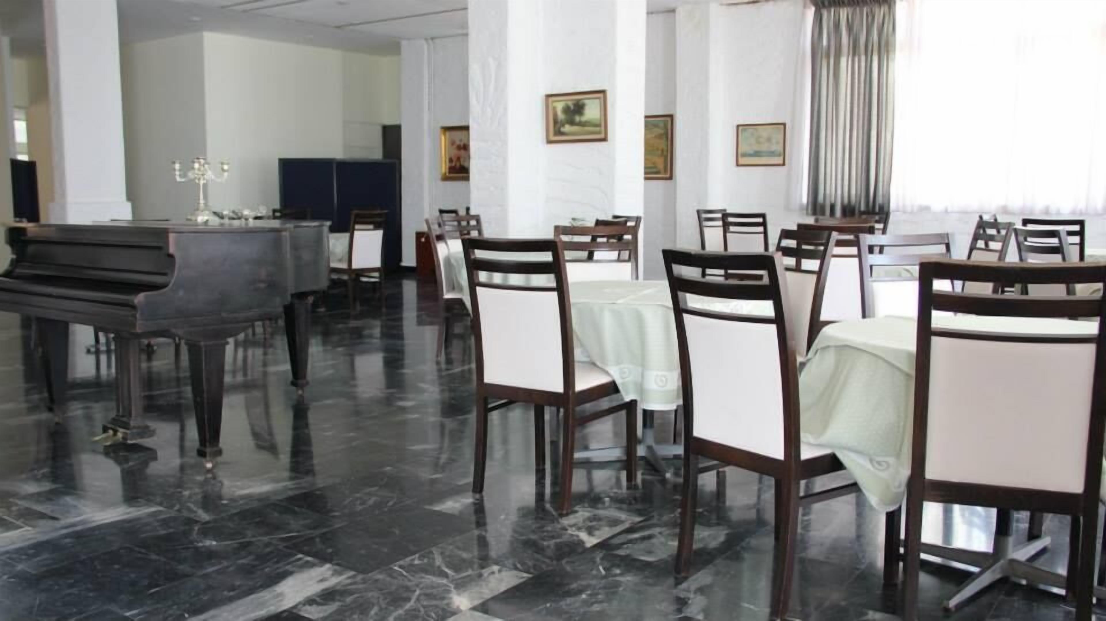 A spacious hotel dining area with marble flooring, multiple tables and chairs, and a grand piano.