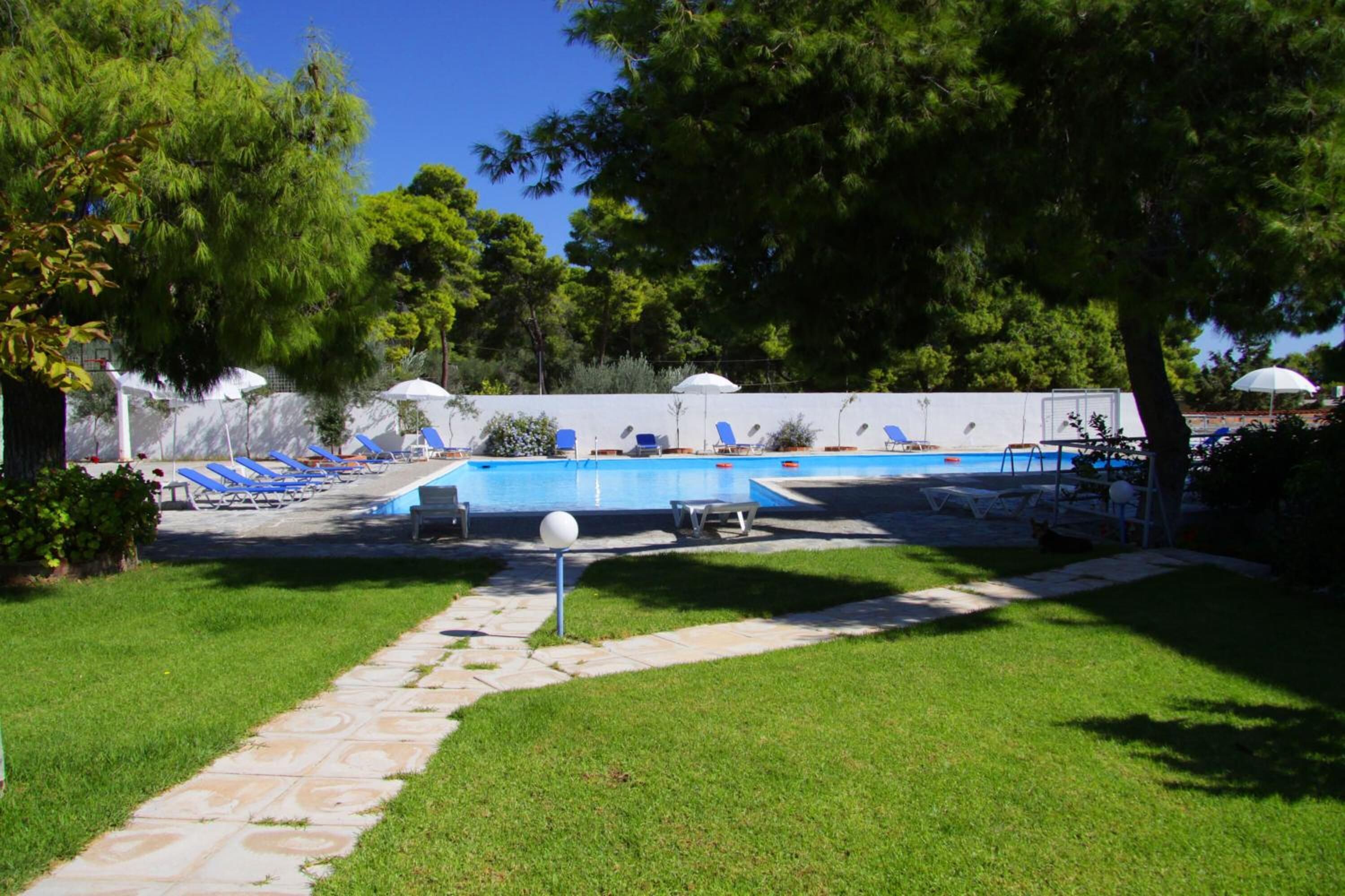 A swimming pool area with lounge chairs and umbrellas, surrounded by trees and a stone pathway.