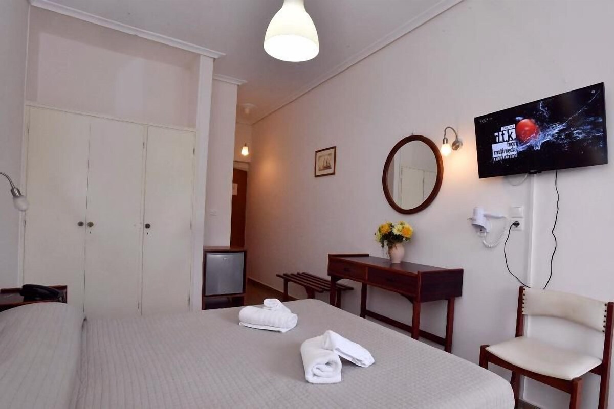 Una habitación de hotel con cama, escritorio, silla, televisor y espejo.