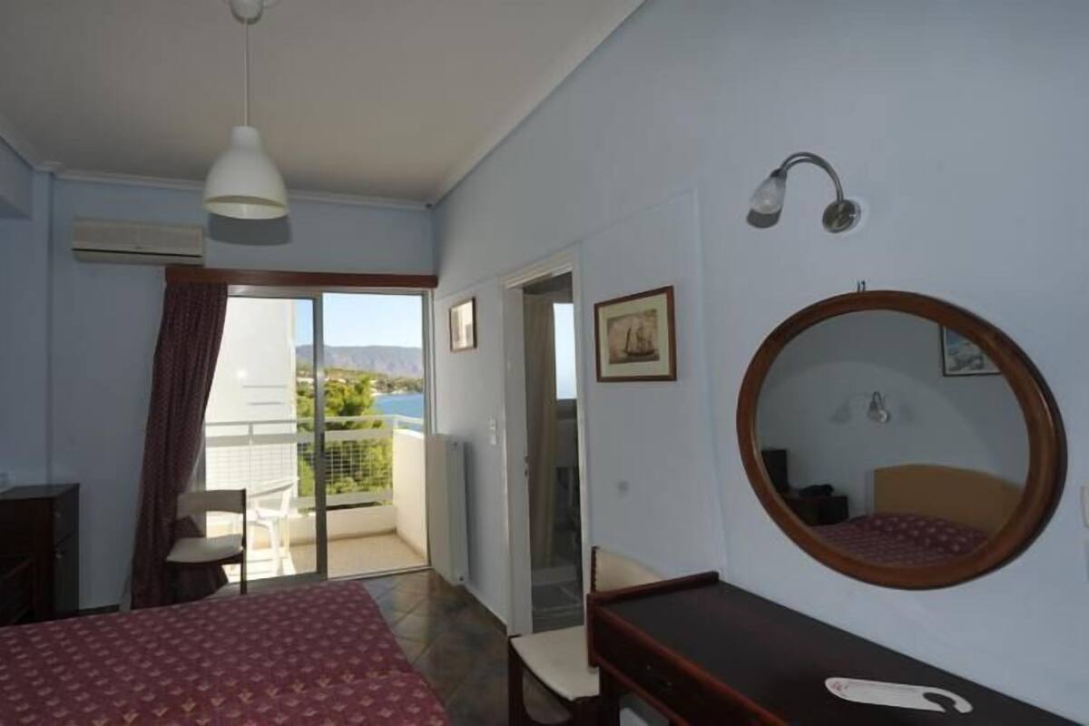 Habitación de hotel con cama, escritorio, silla, espejo redondo y vistas al exterior.