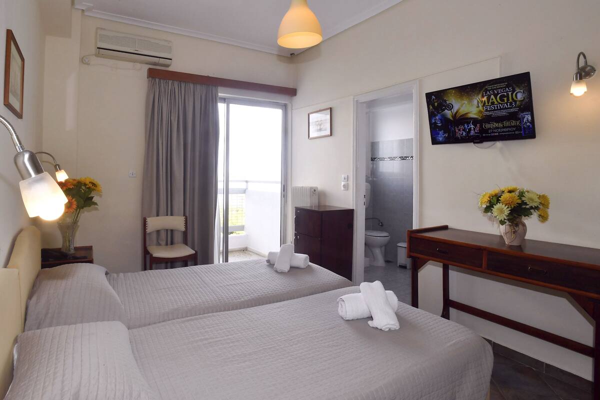 Habitación de hotel con dos camas, un escritorio, un televisor y un baño visible a través de una puerta abierta.