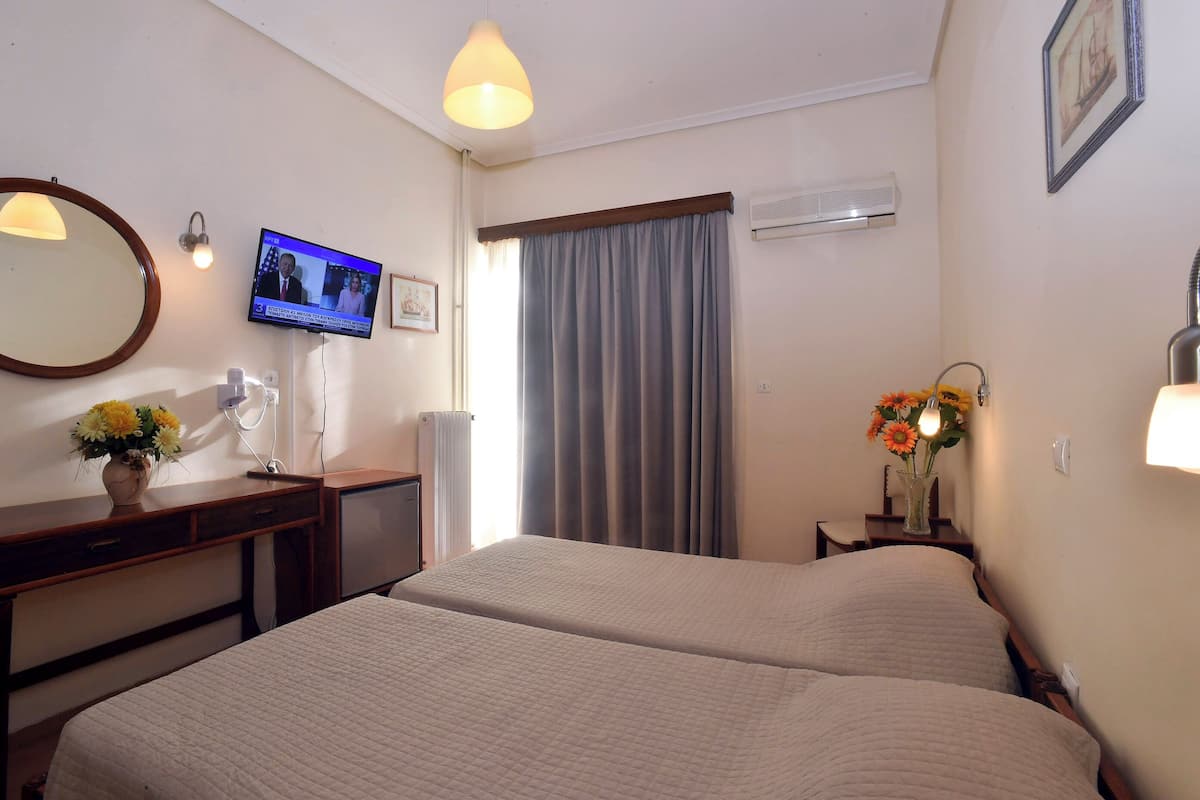 Habitación de hotel con dos camas, televisión, escritorio, espejo, un jarrón con flores y una ventana con cortinas.