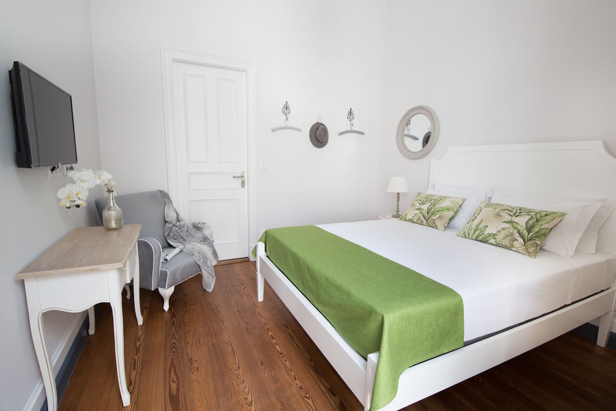 Een slaapkamer met een bed, nachtkastje, stoel, televisie en een deur.