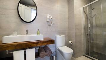 A bathroom with a wooden vanity, a toilet, a glass shower enclosure, and a mirror.