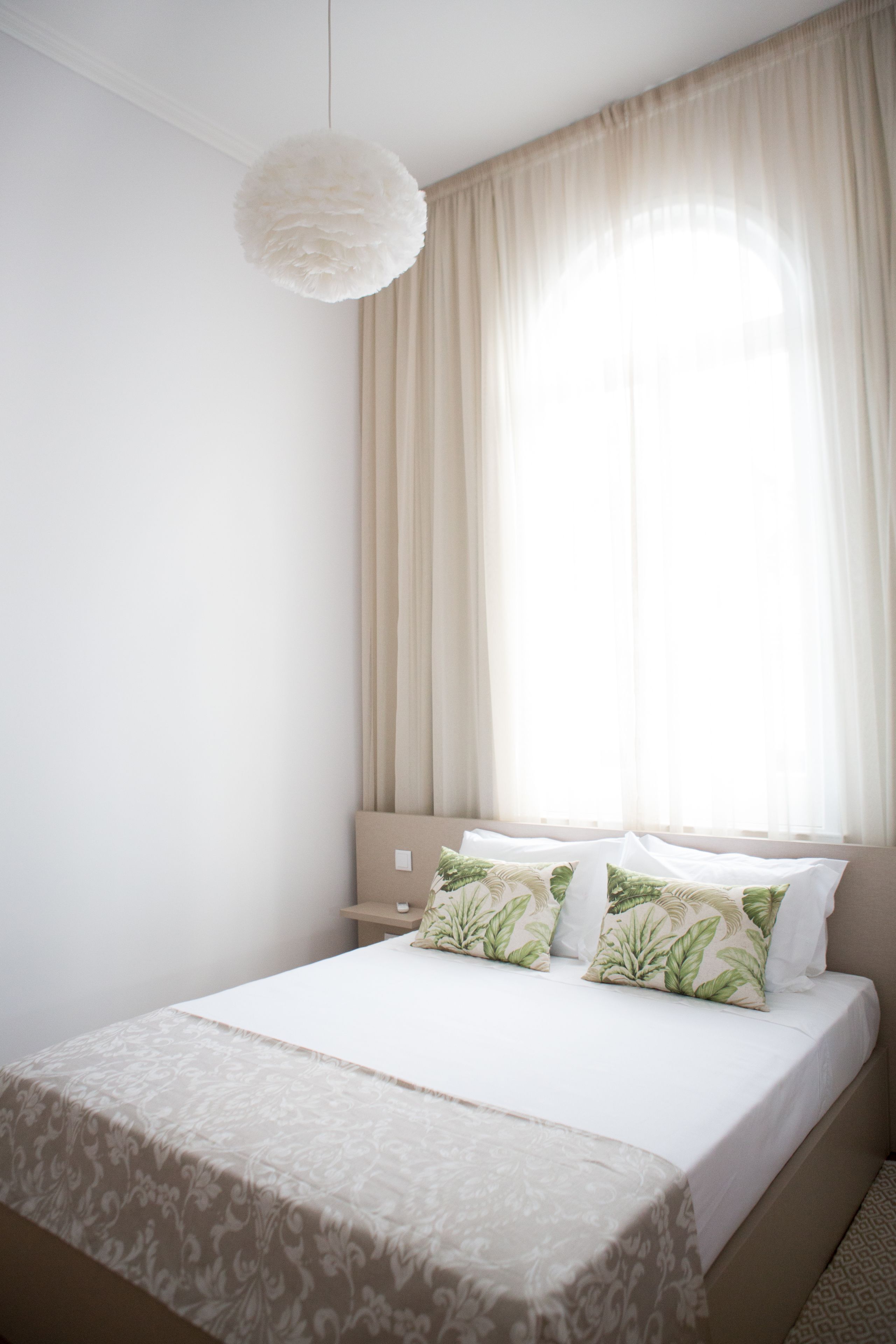 Quarto com cama, luminária pendente e janela com cortinas.