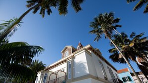 Un edificio blanco con balcón y techo rojo, rodeado de palmeras.