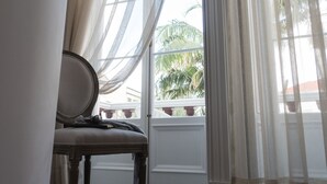 Una habitación con piso de madera, una silla y cortinas translúcidas.