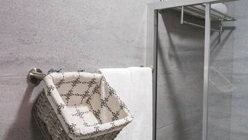 Un baño con cabina de ducha de vidrio, una toalla blanca colgada en la pared y una cesta de mimbre con una toalla.