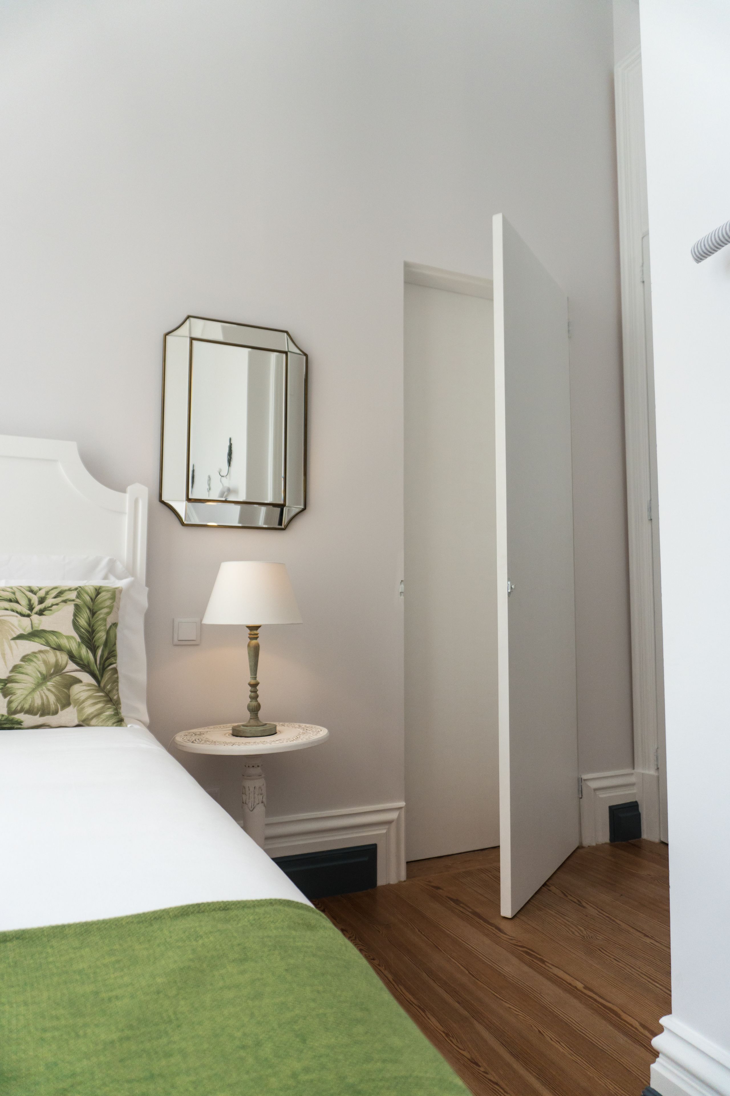 Une chambre à coucher bien rangée, avec un lit, une table de chevet, une lampe et un miroir au mur.