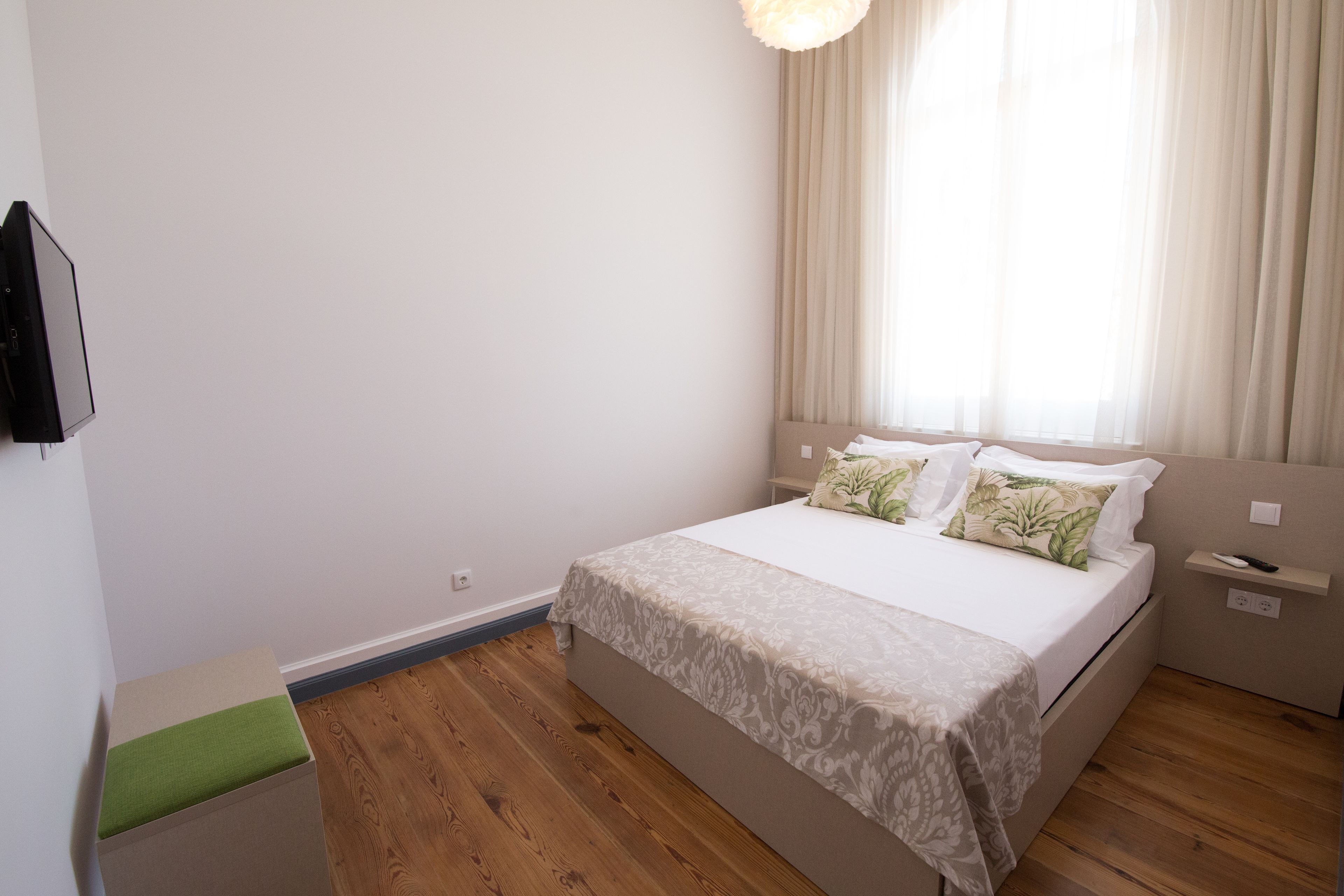 A bedroom with a bed, a bedside table, a nightstand, and a window with curtains.