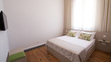 A bedroom with a bed, a bedside table, a nightstand, and a window with curtains.