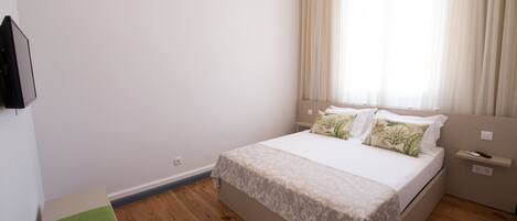 A bedroom with a bed, a bedside table, a nightstand, and a window with curtains.