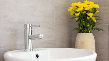 A bathroom sink with a modern faucet and a vase of yellow flowers.