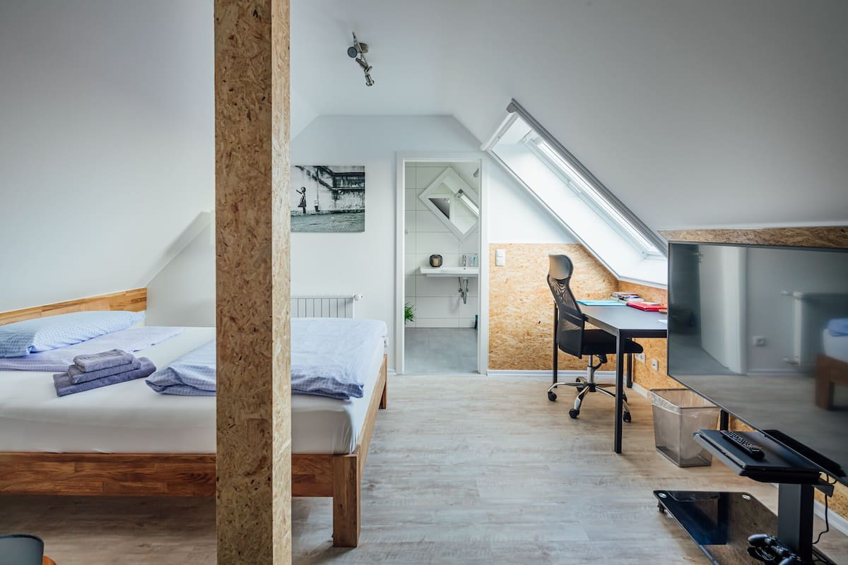 A modern bedroom with a lofted sleeping area, a desk, and a television.
