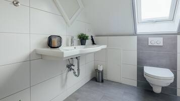 Ein modernes Badezimmer mit einem weißen Waschbecken, einer Toilette und einem Fenster über dem Waschbecken.