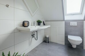A modern bathroom with a white sink, a toilet, and a window above the sink. - Aparthotel Pumpengasse (Wolfsburg)