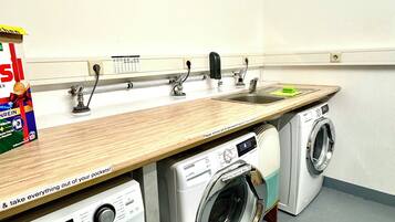 Une buanderie équipée de deux machines à laver à chargement frontal, d’un évier et d’un plan de travail en bois.