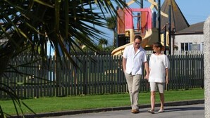 A man and woman walking past a playground with a slide and climbing structure. - Perran View Holiday Park (St. Agnes)
