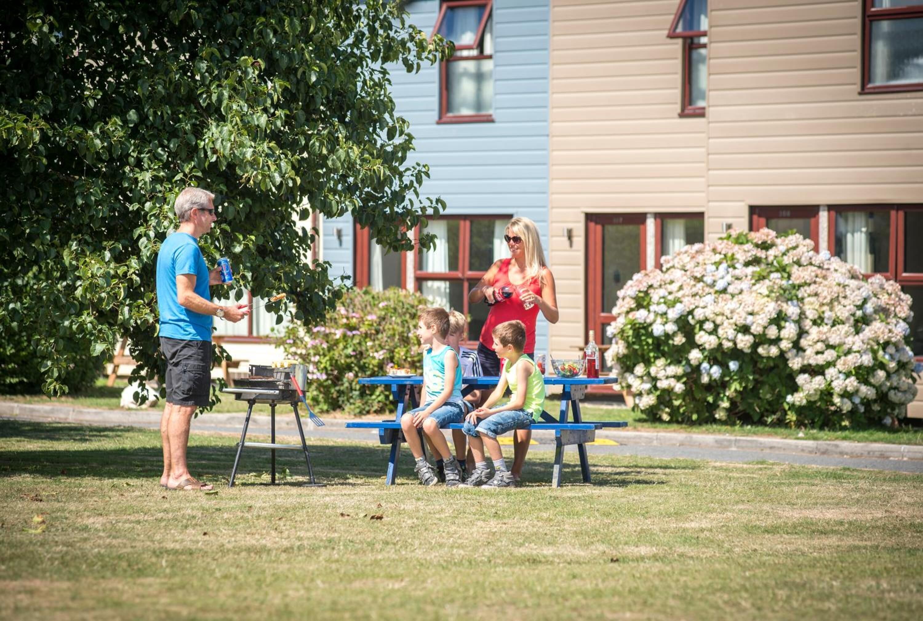 A park with a picnic table where a man is talking to children.