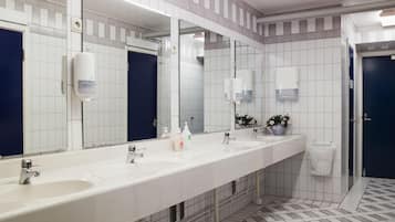 A modern bathroom with white tiled walls, a long counter with two sinks, and a large mirror.