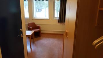 A room with a single chair and a table, a door, and windows with curtains.