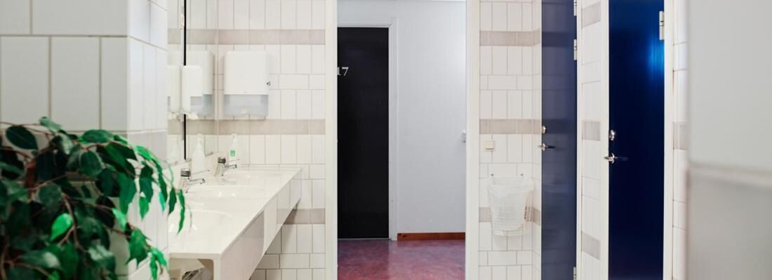 Un baño de hotel con pared de azulejos blancos, un lavamanos y una puerta que da a otra habitación.