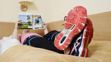 A person lying on a bed with a magazine, wearing a pair of athletic shoes with a distinctive red sole.