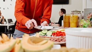 A breakfast buffet with various fruits and vegetables, a coffee machine, and juice dispensers. - Hotell Sport & Rest (Pitea)